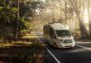 A white motorhome traveling down the road in a forest setting.