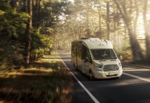 A white motorhome traveling down the road in a forest setting.