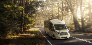 A white motorhome traveling down the road in a forest setting.