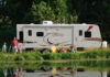 Family enjoying the RV camping experience by a pond at their campground. KZ-RV Spree Ultralight travel trailer, side view.