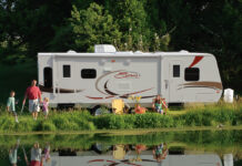 Family enjoying the RV camping experience by a pond at their campground. KZ-RV Spree Ultralight travel trailer, side view.