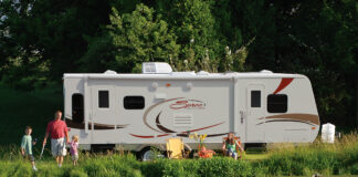 Family enjoying the RV camping experience by a pond at their campground. KZ-RV Spree Ultralight travel trailer, side view.