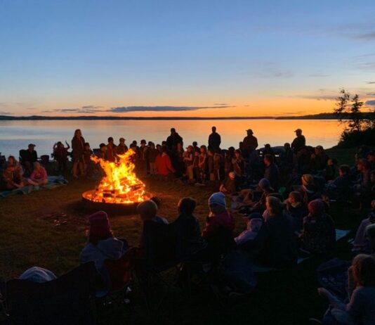 Scouts gather on a beach, around a campfire.