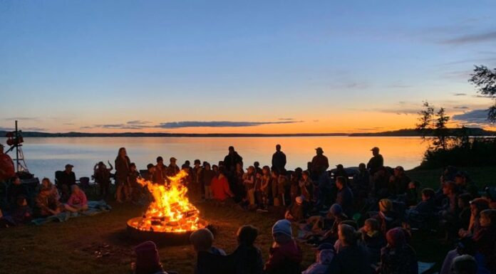 Scouts gather on a beach, around a campfire.