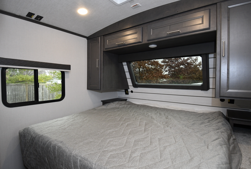The Keystone RV Cougar 25MLE travel trailer bedroom has a king size bed with plenty of storage above and below the bed
