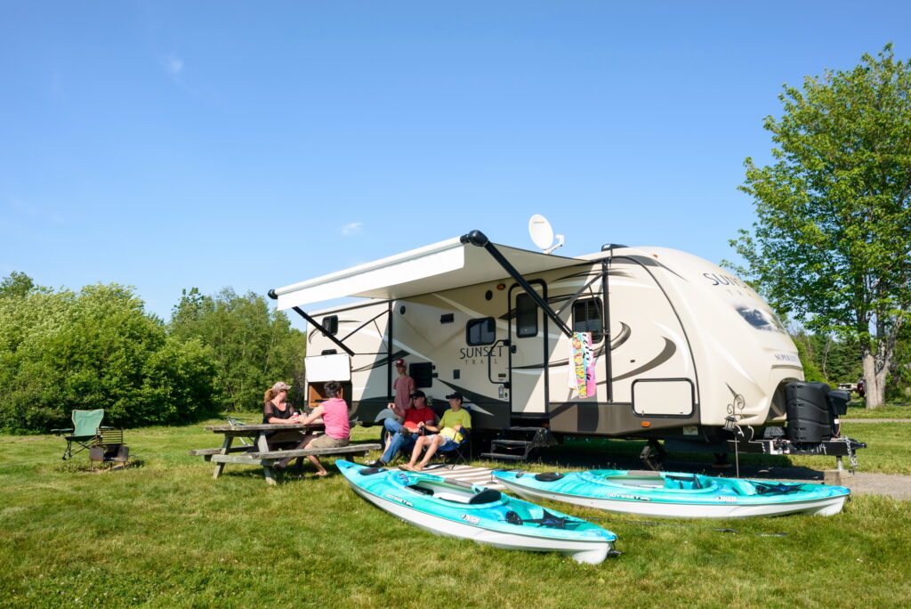 A Family sitting in front of their recreational vehicle at their campsite in the South Kouchibouguac
Campground, Kouchibouguac
National Park, New Brunswick, Canada. Photo © Parks Canada / Nigel Fearon